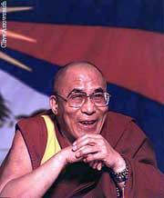 Photograph of His Holiness the 14th Dalai Lama before a Tibetan flag; date and location unknown.
